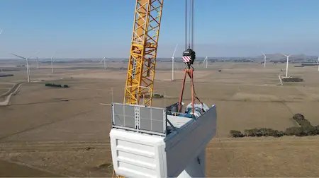 A crane elevating the top part of a windmills in a windmills field.